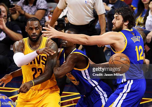 LeBron James of the Cleveland Cavaliers passes around Harrison Barnes and Andrew Bogut of the Golden State Warriors in the third quarter during Game...