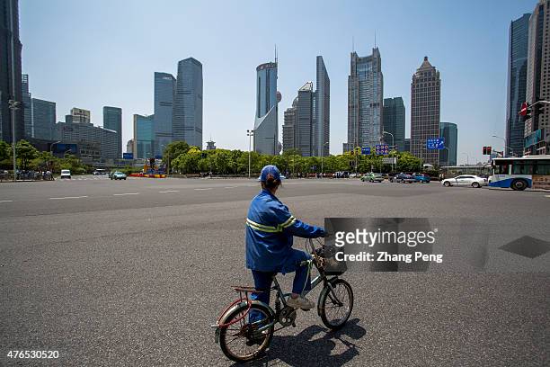 City sanitation worker stops at a crossroad looking at the skyscrapers in Lujiazui. Located in the Pudong New District on the eastern bank of Huangpu...