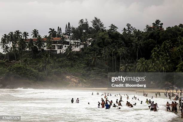 Visitors relax in the surf as the Leela Kovalam Hotel stands on a cliff in the background at Kovalam beach in Kovalam, Kerala, India, on Sunday, May...