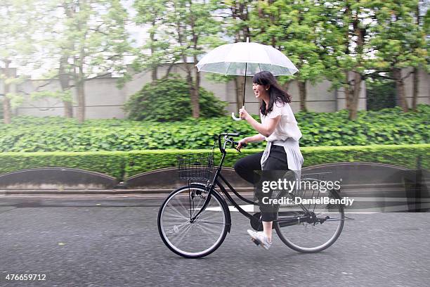 young japanese woman riding bicycle on rainy day in tokyo - asia rain stock pictures, royalty-free photos & images