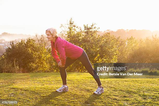 senior female runner stretching legs outdoor. - sunny morning stock pictures, royalty-free photos & images