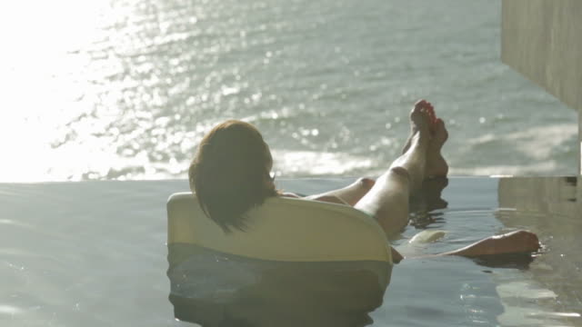 Woman relaxing in chair in infinity pool overlooking ocean