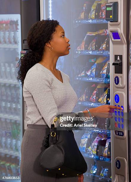 mixed race woman buying snack from vending machine - vending machine stock-fotos und bilder