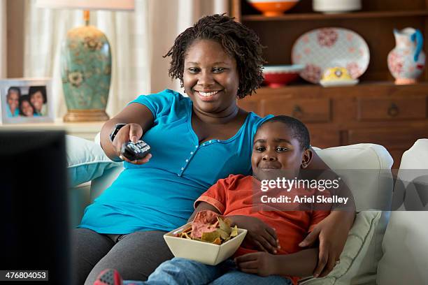 black mother and son watching television together - family eating potato chips stock pictures, royalty-free photos & images