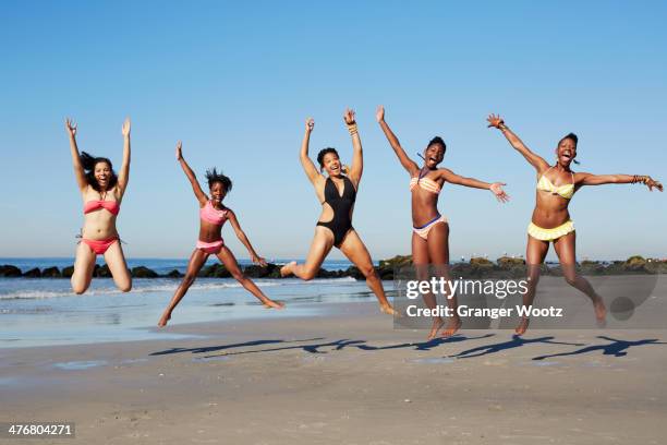 women jumping for joy on beach - swimsuit stock-fotos und bilder