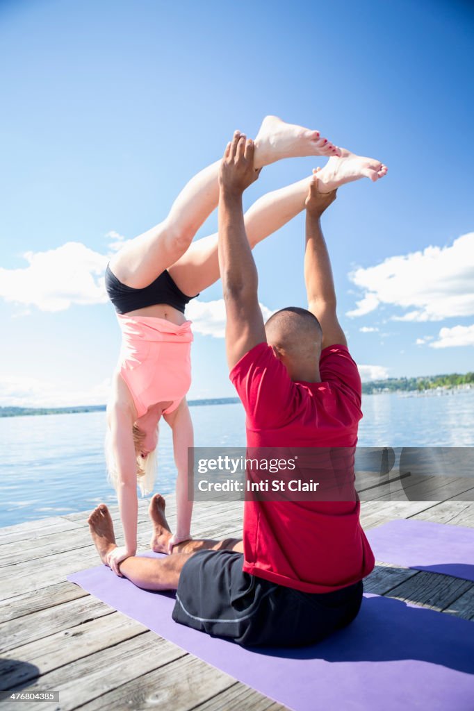 Caucasian couple practicing acroyoga on wooden dock