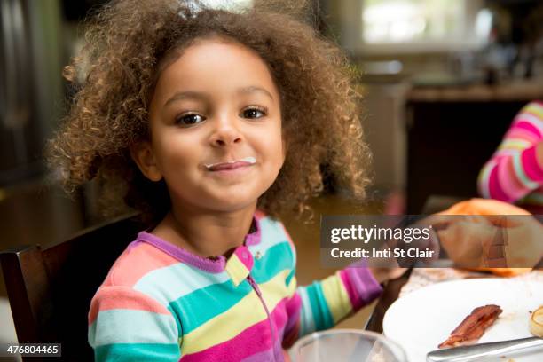 mixed race girl with milk mustache at table - milk moustache stock-fotos und bilder