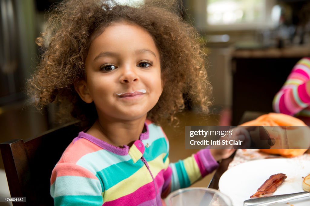 Mixed race girl with milk mustache at table