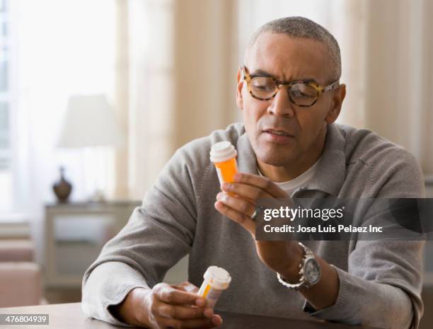mixed race man examining prescription bottles - prescription medicine imagens e fotografias de stock