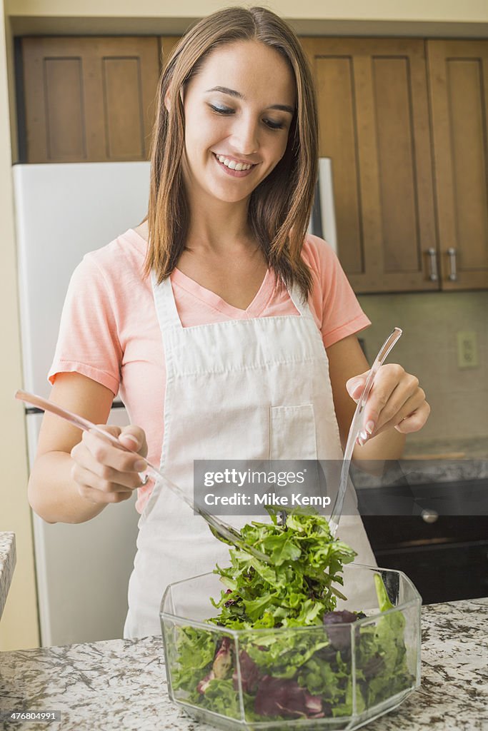 Caucasian woman tossing salad in kitchen