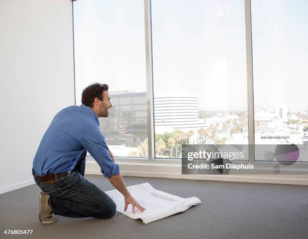 hispanic businessman examining blueprints in office - kneeling stock pictures, royalty-free photos & images