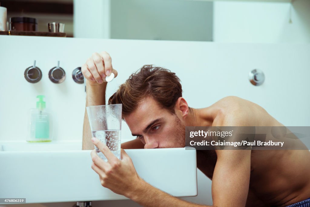 Verkaterter Mann, der Brausetabletten im Badezimmer beobachtet
