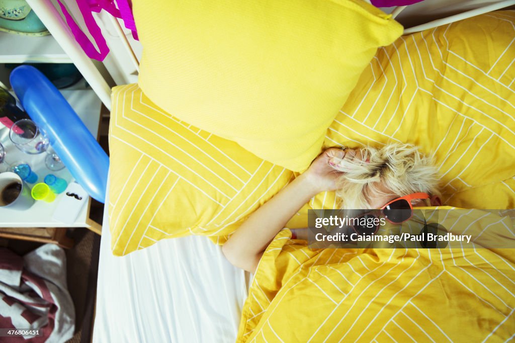 Woman wearing sunglasses in bed after party