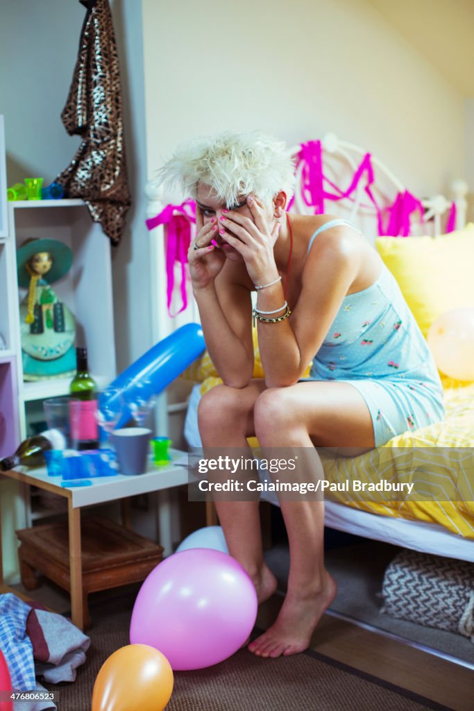 Hungover woman rubbing face on bed the morning after a party