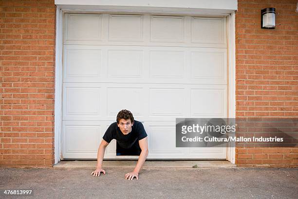 young man crawling through hole in garage door - trappen photos et images de collection