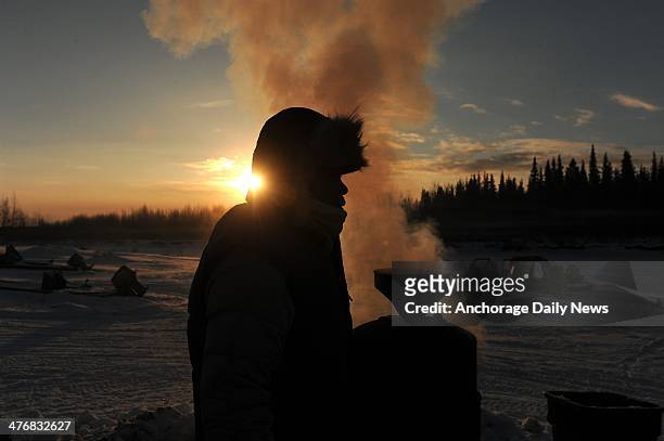 Iditarod musher Newton Marshall gets hot water from the wood fired heater at the Nikolai checkpoint during the 2014 Iditarod Trail Sled Dog Race at...