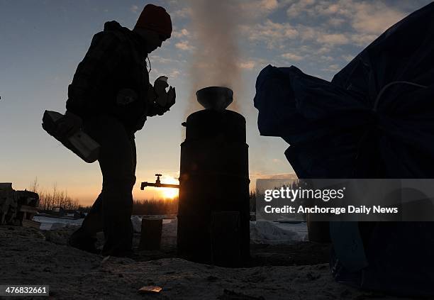 Phil Runkle brings an armful of wood to the water heater at the Nikolai checkpoint during the Iditarod Trail Sled Dog Race at sunrise on Wednesday,...