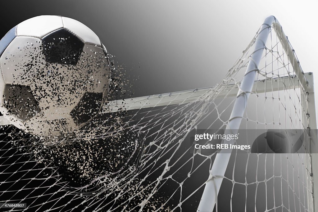 Studio shot of football powering through goal netting