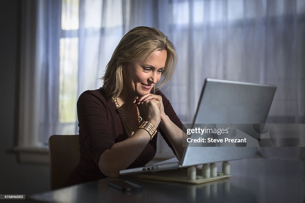 Mature woman sitting at home using laptop