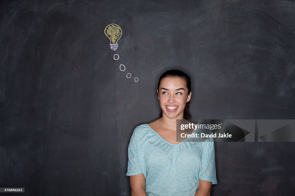 Young woman by blackboard with lightbulb