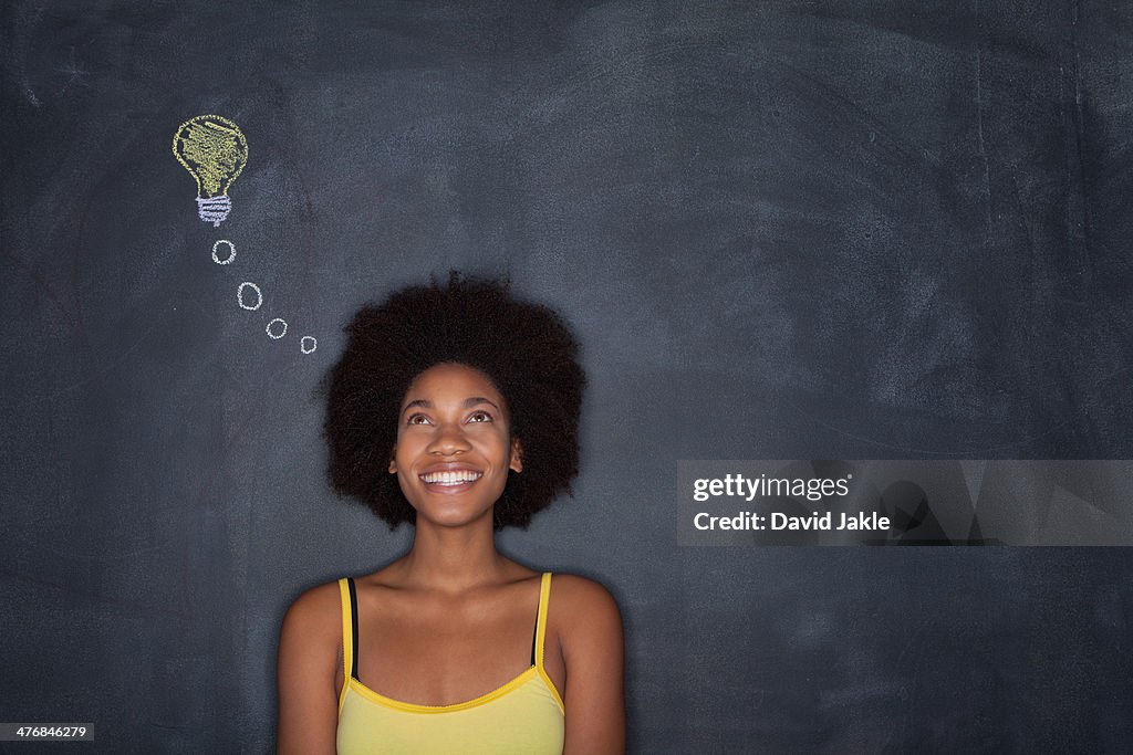 Young woman by blackboard with lightbulb