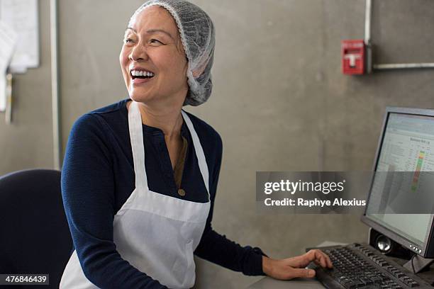 woman wearing apron and hairnet using computer - haarnet stockfoto's en -beelden