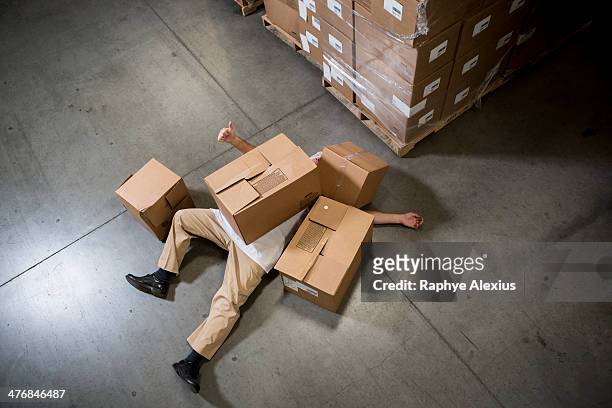 man lying on floor covered by cardboard boxes in warehouse - crush foot stock pictures, royalty-free photos & images
