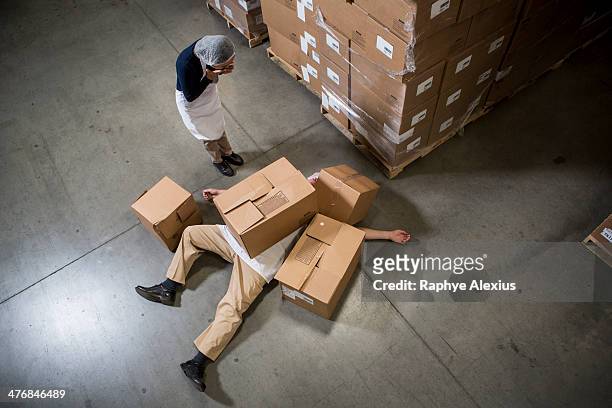 woman looking at man lying on floor covered by cardboard boxes in warehouse - crush foot stock pictures, royalty-free photos & images