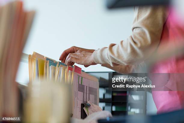 senior woman looking through filing cabinet - filing stock-fotos und bilder