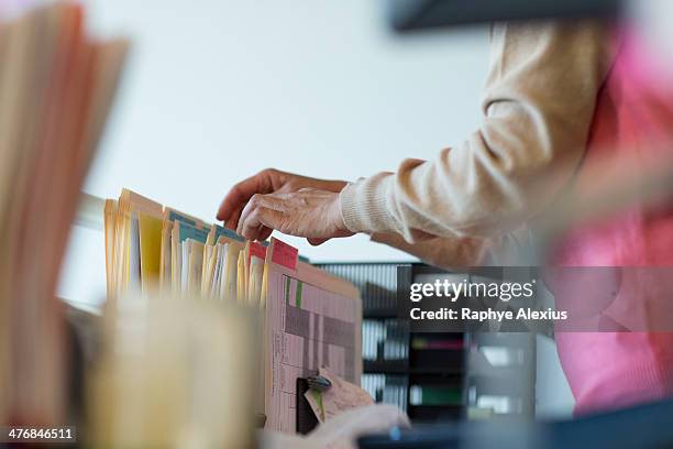 senior woman looking through filing cabinet - filing cabinet photos et images de collection