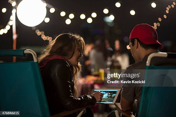 young couple looking at digital tablet at rooftop barbecue - tablet paar sommer stock-fotos und bilder