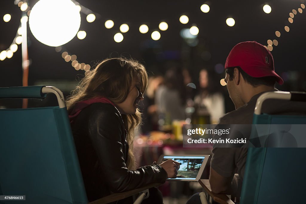 Young couple looking at digital tablet at rooftop barbecue