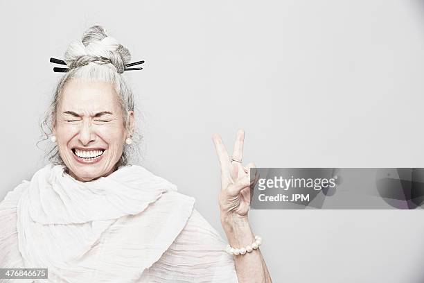 studio portrait of sophisticated senior woman making victory sign - grey hair cool woman stock-fotos und bilder