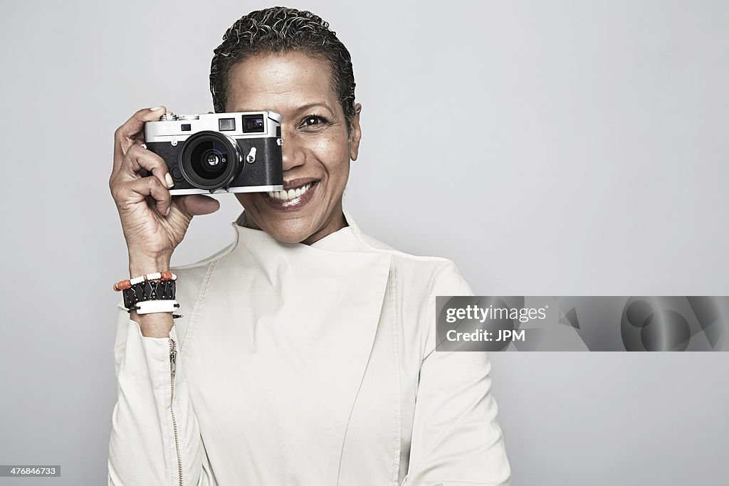 Studio portrait of happy mature woman holding up camera