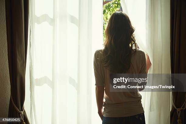 young woman peeking out from net curtains - female back stock pictures, royalty-free photos & images