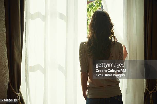 young woman peeking out from net curtains - back view bildbanksfoton och bilder