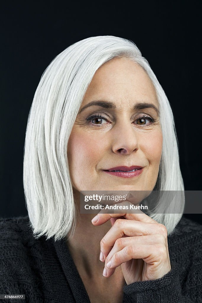 Grey haired mature woman with hand on chin.