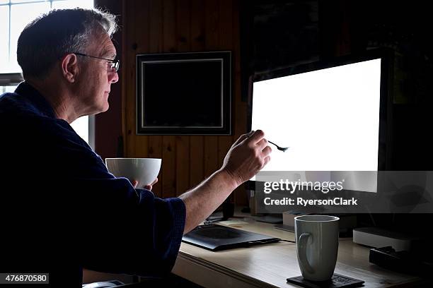senior man eating breakfast in front of computer. - staring at screen stock pictures, royalty-free photos & images