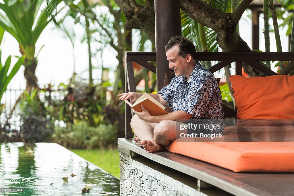 Canadian Man Reading Poolside on Summer Vacation in Bali Cabana