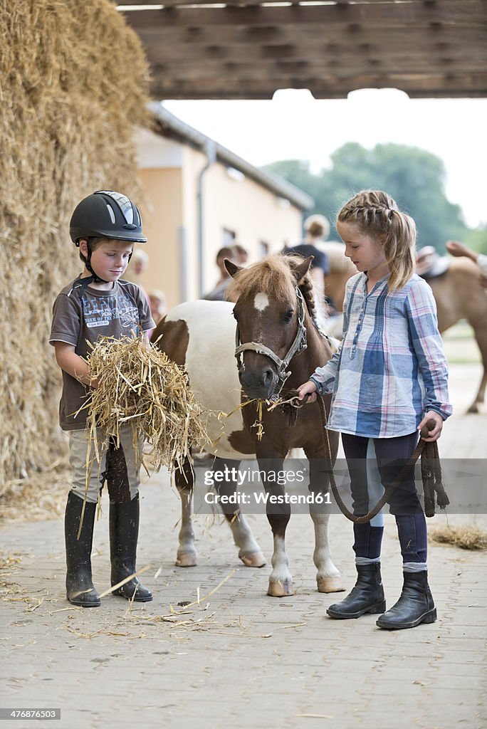 Germany, NRW, Korchenbroich, Boy and Girl at riding stable with mini shetland pony