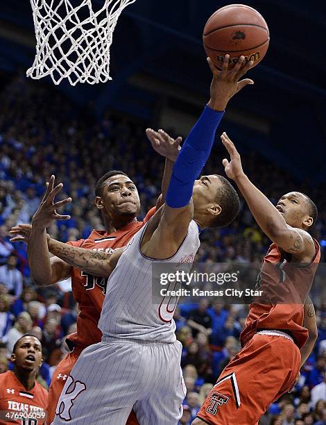 Kansas' Frank Mason, middle, is hammered by Texas Tech's Aaron Ross, left, on his way to the bucket during the first half at Allen Fieldhouse in...