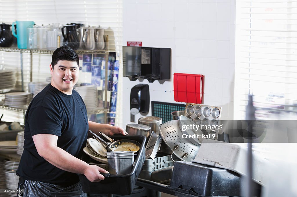Asian man in restaurant carrying tub of dirty dishes