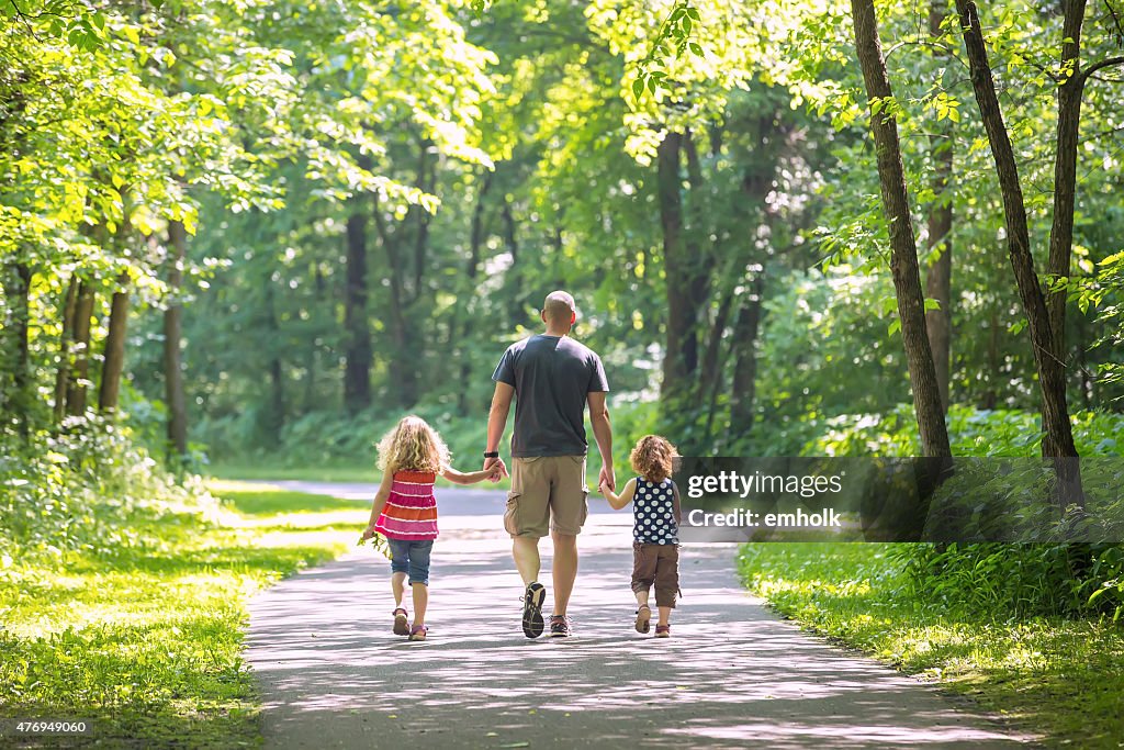 Father And Two Daughters Walking Through Woods at Park