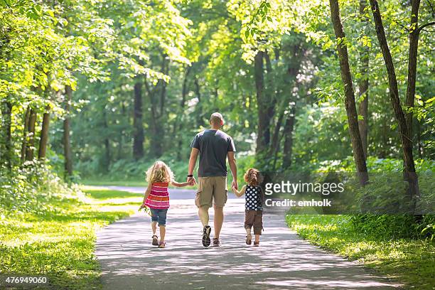 father and two daughters walking through woods at park - footpath stock pictures, royalty-free photos & images