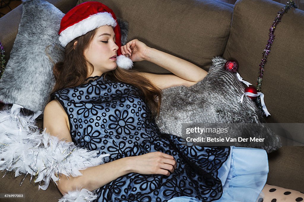 Young woman sleeping on sofa wearing christmas hat