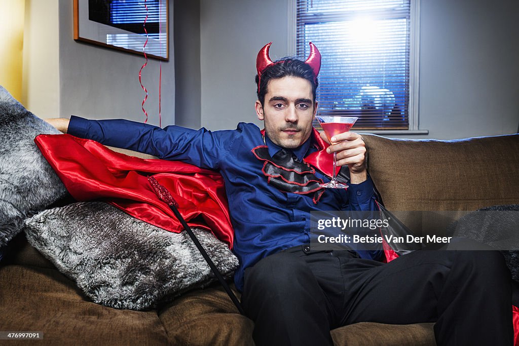 Halloween devil relaxing on sofa with cocktail.