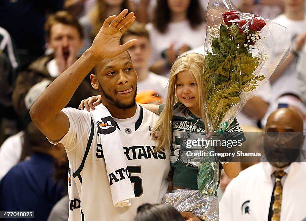 Adreian Payne of the Michigan State Spartans walks on the floor for Senior night with Lacey Holsworth, a 8-year-old from St. Johns Michigan who is...