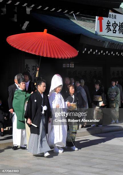 Bride and groom leads their wedding entourage at a Shinto wedding at the Meiji-Jingu shrine in the Harajuku district of Tokyo. The couple walks under...