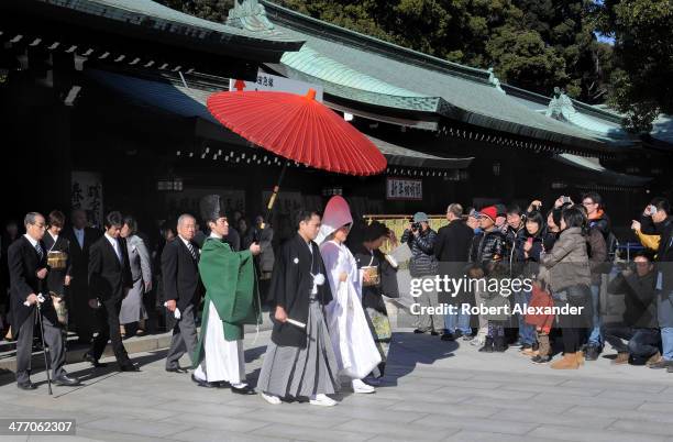 Bride and groom leads their wedding entourage at a Shinto wedding at the Meiji-Jingu shrine in the Harajuku district of Tokyo. The couple walks under...