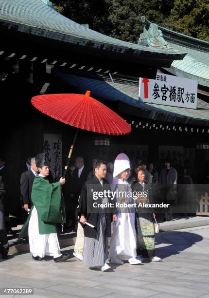 Bride and groom leads their wedding entourage at a Shinto wedding at the Meiji-Jingu shrine in the Harajuku district of Tokyo. The couple walks under...